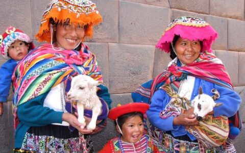 two women in colorful local clothing with two goats and two children in peru