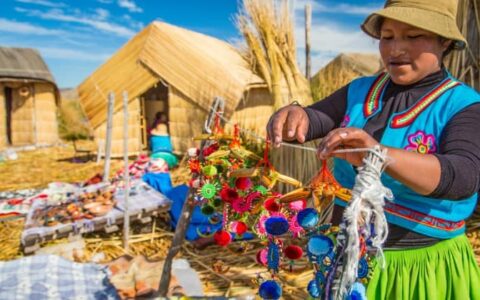 peruvian woman in colorful clothing hangs crafts at market on peru highlights trip
