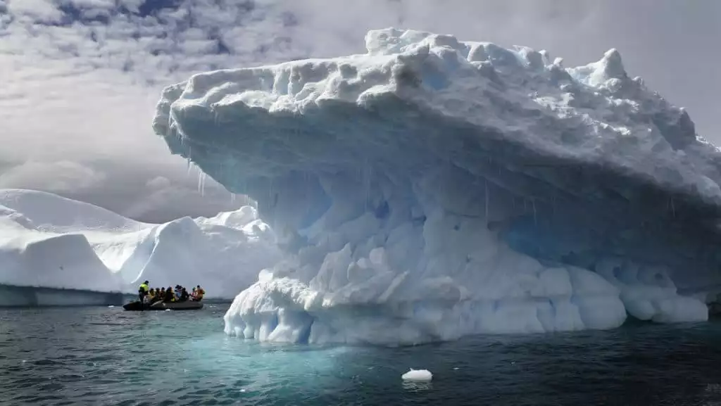 Antarctica travelers Zodiac cruising amongst massive icebergs in icy blue and turquoise waters on a sunny day in Port Charcot.