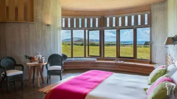A room at Explora Rapa Nui with lots of windows, bed and tables and chairs.
