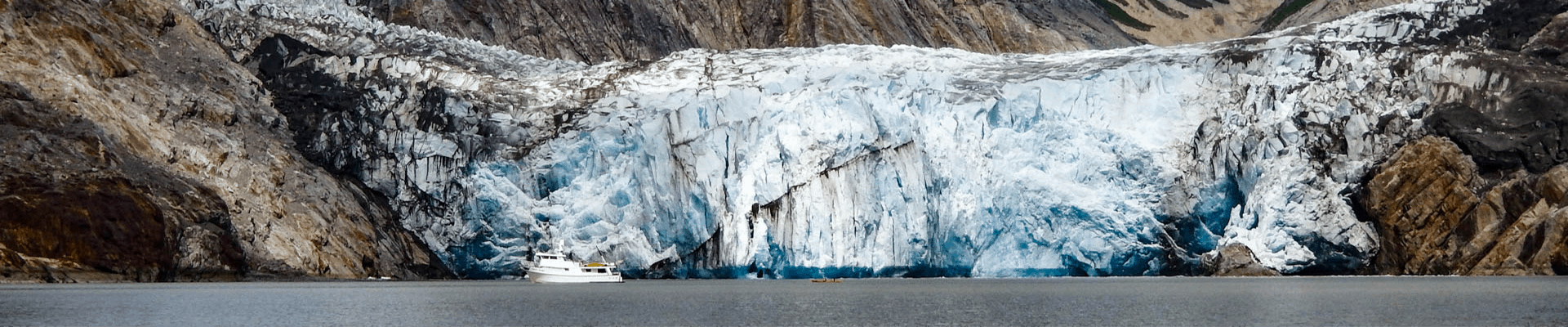 A blue-white glacier in a calm bay in Alaska with a small ship in front of the glacier