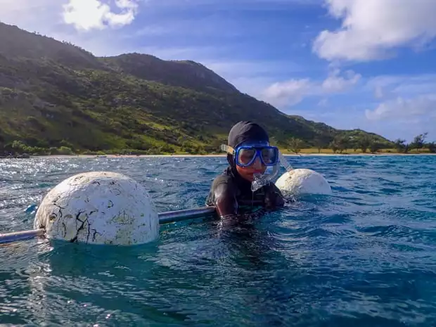 A child in snorkel gear holding on a float taking a break from snorkeling on a small ship cruise.