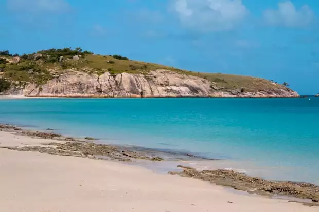 A remote sandy beach in Australia on a small ship cruise. with an island in the background.