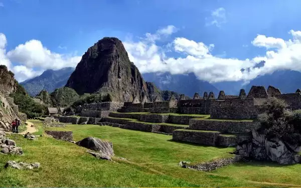 adventure travelers walk and see machu picchu and its terraces on a sunny day with puffy clouds in the distance