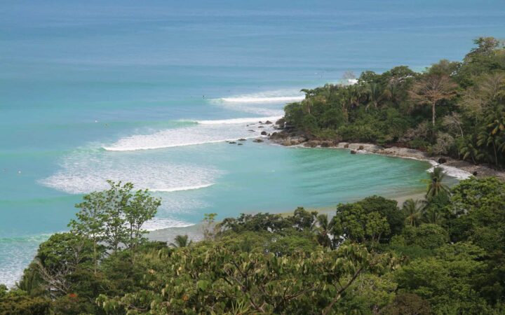 showcasing the costa rica climate in summer looking down on a perfect sunlit ocean with waves touching a green rainforest set against the beach