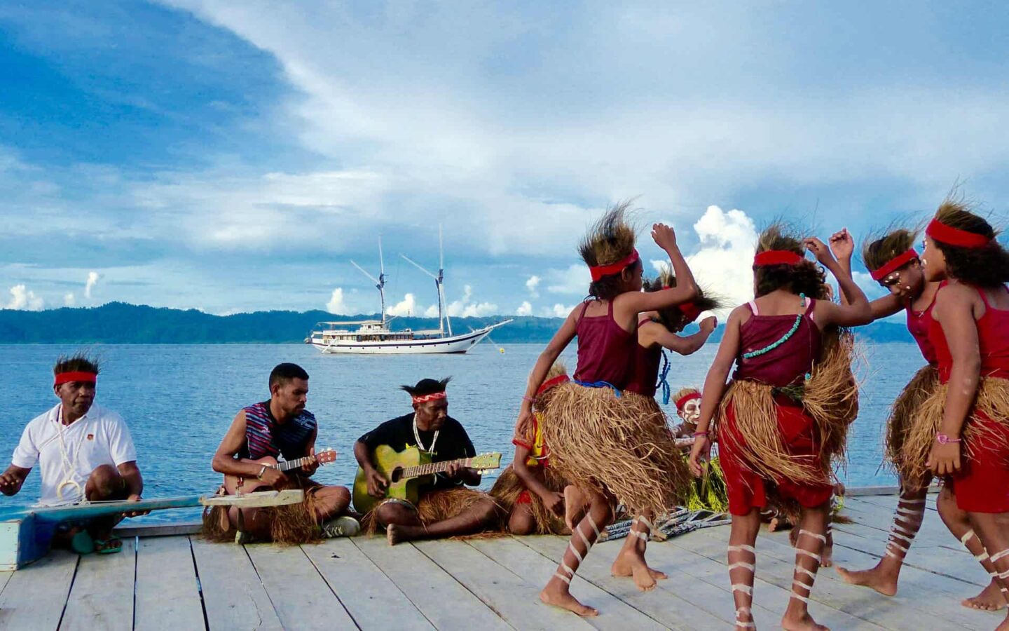 indigenous indonesian people dancing with a small ship in the distance