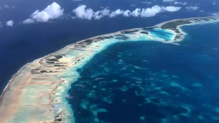 Aerial view of a string of Tahitian islands & coral reef surrounded by turquoise & deep blue water on the Easter Island to Tahiti cruise.