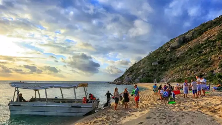 adventure travelers relax on a desolate beach at sunset with a skiff anchored on shore during the great barrier reef australia cruise