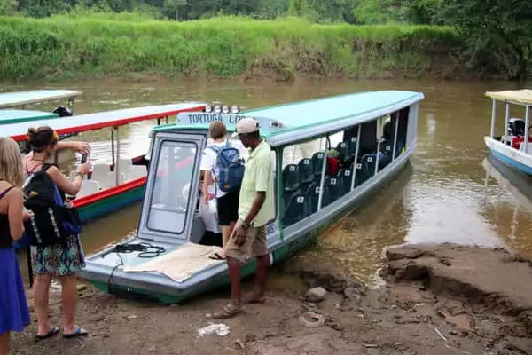 Families of travelers embarking on a covered open air boat on a river in Costa Rica.
