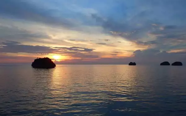 calm ocean at sunset seen from a small ship cruise with clouds across the sky and small islands on the water