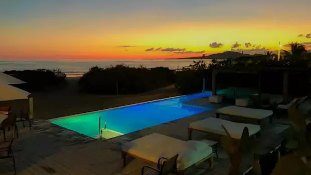 Yellow and orange sunset from a lodge with a pool and lounge chairs.