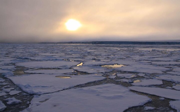showcasing the arctic climate with sun peaking through clouds and patches of sea ice floating from the foreground to the horizon