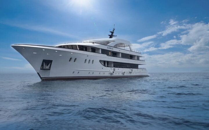 View from water, of a white yacht sitting in calm water on a sunny day.