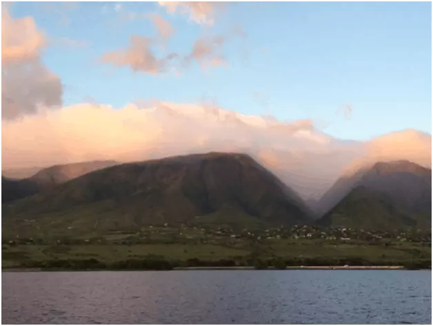 Green mountains enshrouded in pink clouds during a sunset from the viewpoint of the ship