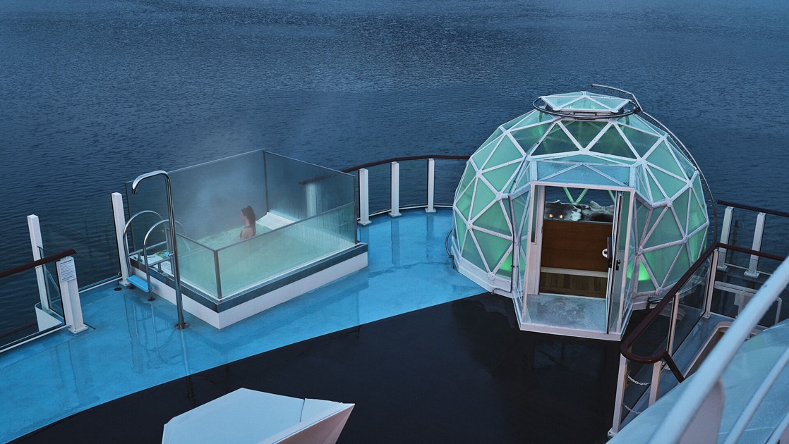 Glass geodesic dome with purple interior lighting sits beside a glass-walled small pool on deck of National Geographic Resolution.