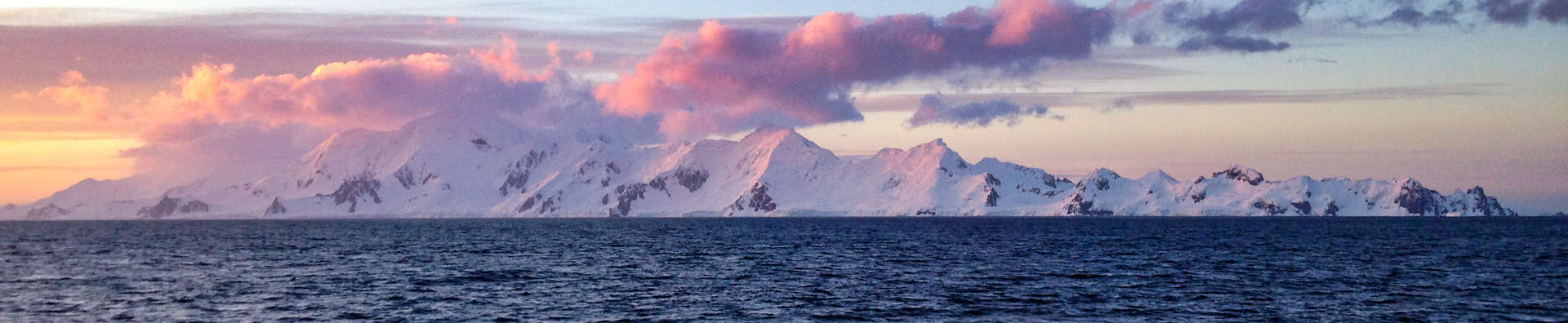 antarctica mountain range with calm ocean in the foreground and illuminated pink clouds above
