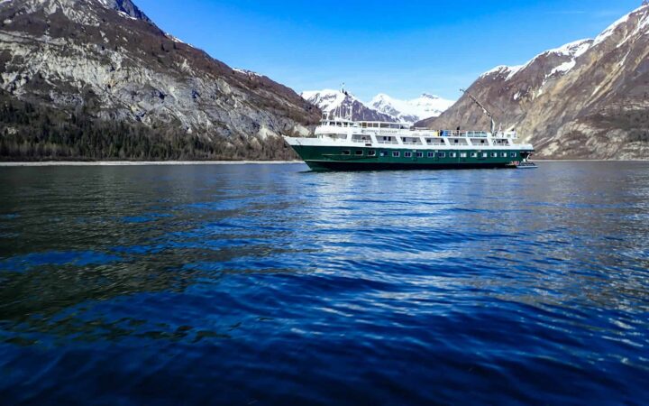 Wilderness Adventurer ship sailing through glacier bay national park on a sunny calm day with blue water and sky.