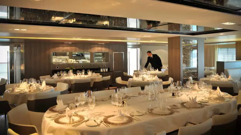 Gastronomic restaurant aboard Le Boreal white linens cover the tables with plate settings and a man in a suit pouring water