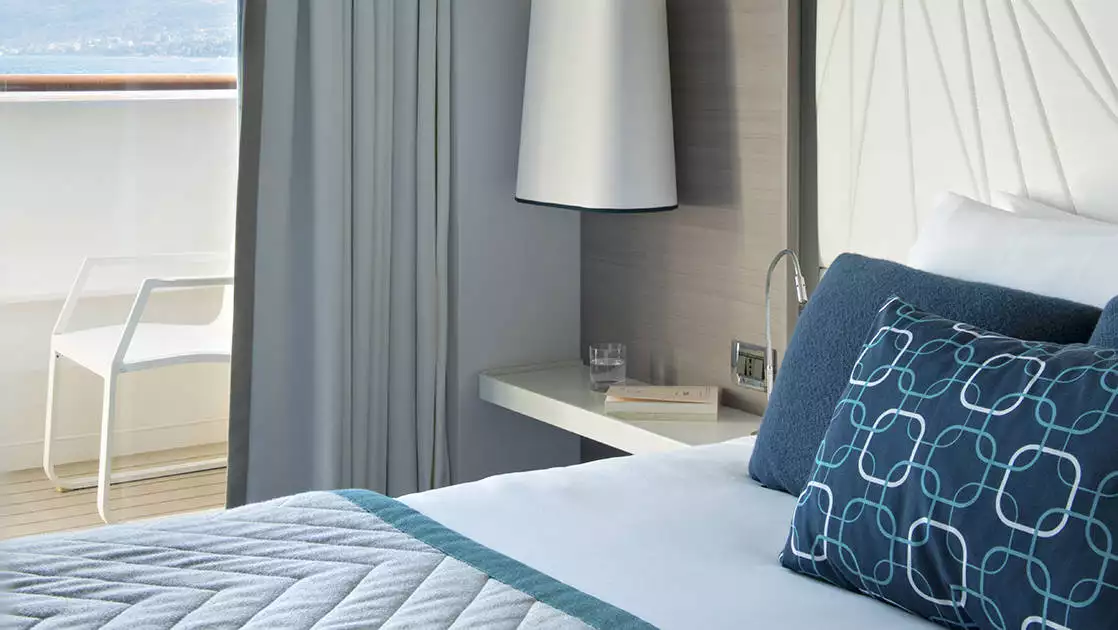 Deluxe Stateroom aboard Le Lyrial expedition ship, with blue-&-ivory decor, bed, bedside table & lamp & private balcony.