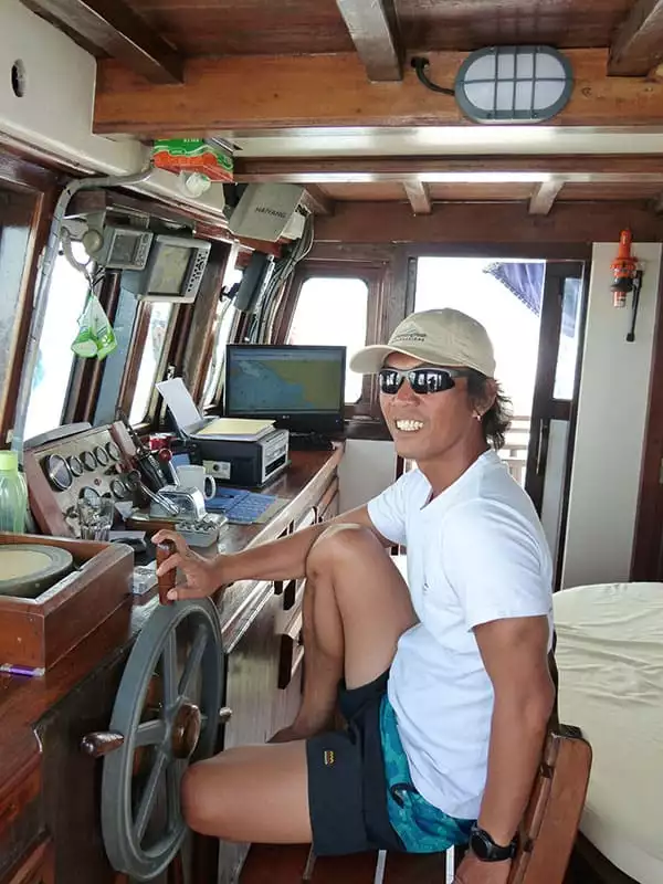 the captain of the small indonesia ship the ombak putih sits in his chair at the wheel of the ship inside the bridge