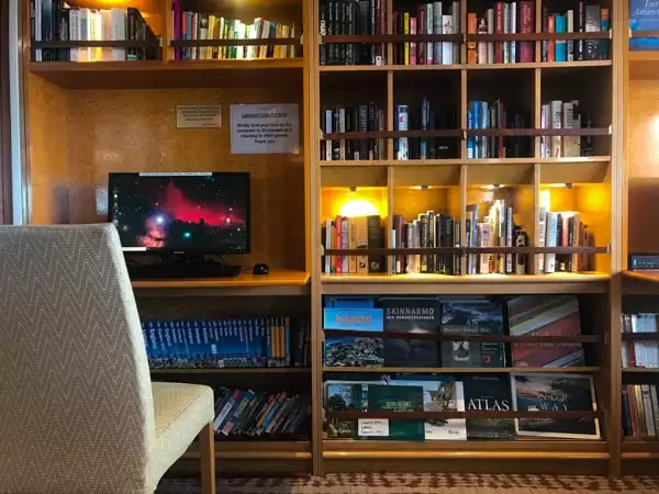 The library aboard hebridean sky polar expedition vessel a chair with a wall full of cubbies and books, and a computer sits on a desk.
