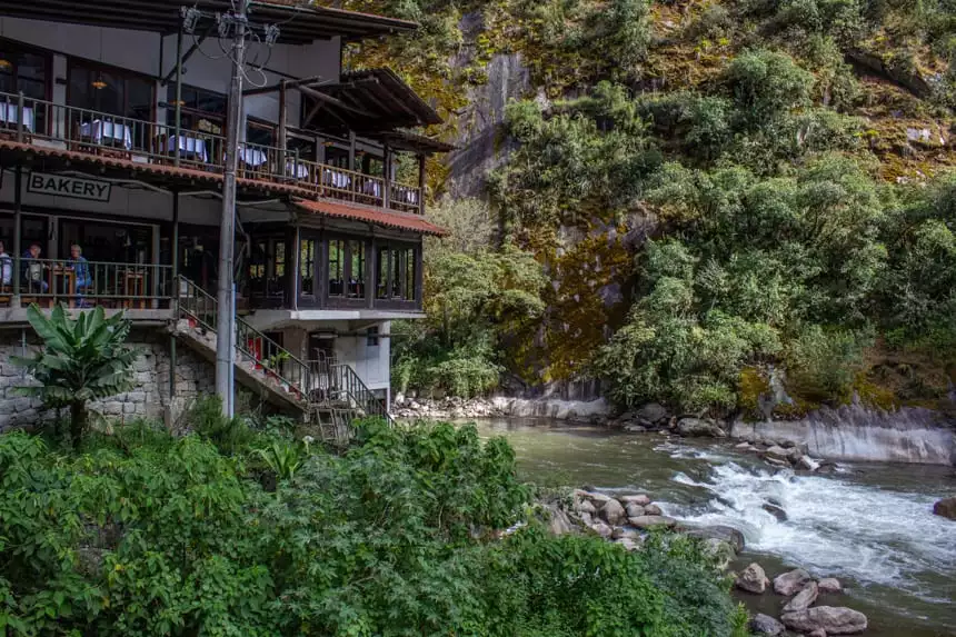 A view from the Urubamba River in Aguas calientes, Peru. Green lush mountain side is split from a building by the river.