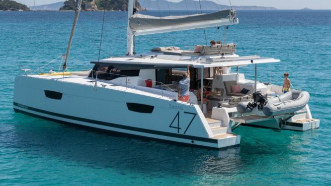 The exterior of Tranquilo Belize charter ship, passengers lounge about on the all white deck as it floats in the teal ocean, her grey sails are lowered