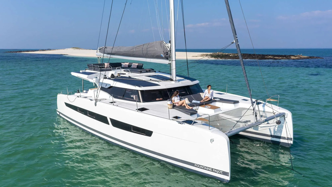 Large catamaran sailing through beautiful waters with two guests sitting at the helm relaxing aboard second wind