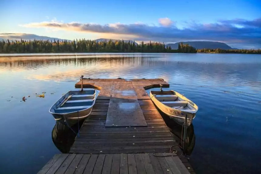 a dock floats with two metal boats tieds up to it at Winter lake Lodge in Alaska the glow of the setting sun is seen over the forest of trees on the opposite side of the lake