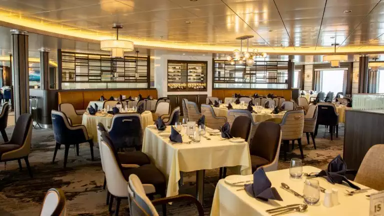 A beautiful dining room with white cloth covered tables set for a meal aboard the Sylvia Earle as it sails the polar seas
