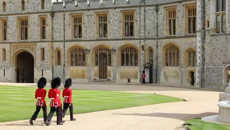 Royal guards in tall black furry hats, black pants & red coats approach Windsor Castle during the Classic England River Thames Cruise.