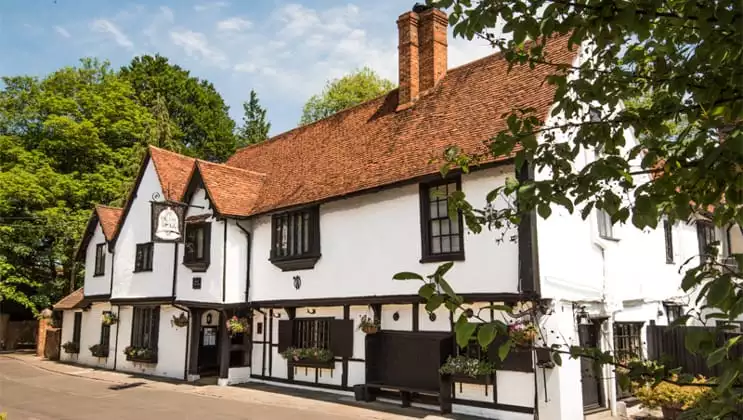 A white-&-brown Tudor Mansion with terracotta roof tiles, seen on a sunny day during a London river cruise.