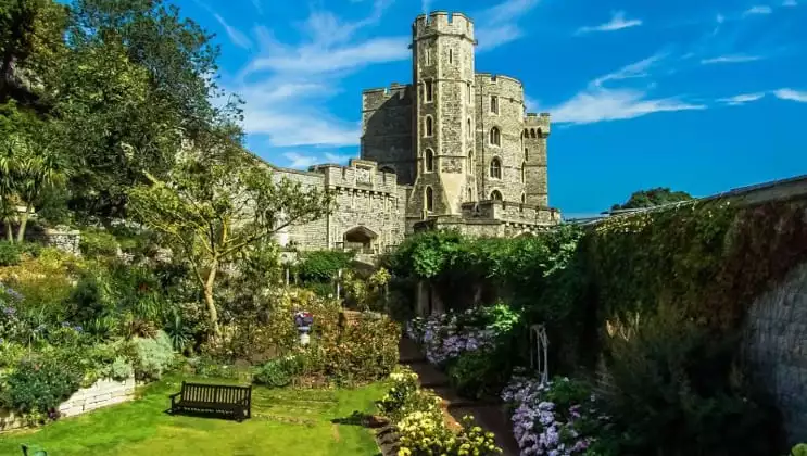Immaculate gardens leading up to tall Windsor Castle, seen on a sunny day during the Classic England River Thames Cruise.