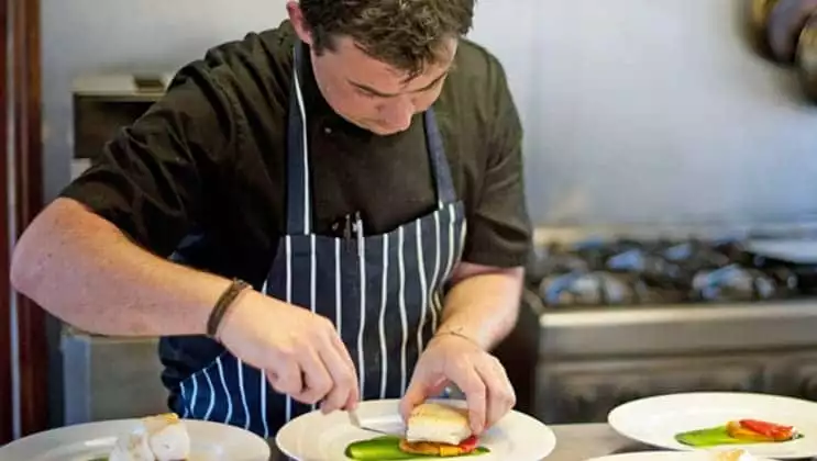 Chef preparing plates of fancy cuisine in the kitchen of England barge Magna Carta.