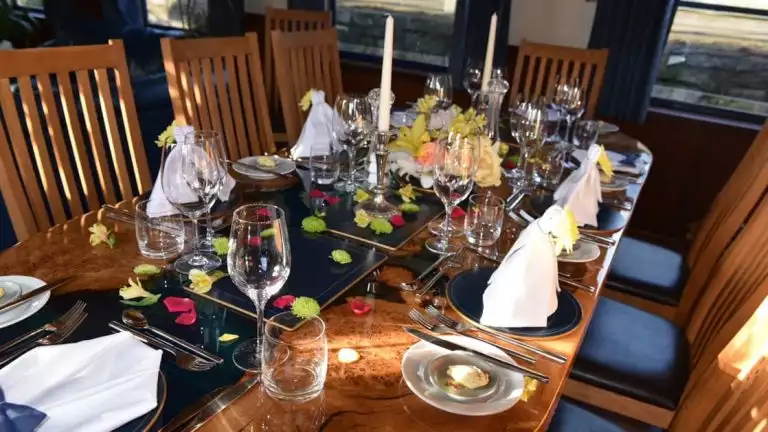 10-guest dining table set for dinner with white linens, candles, flowers & wine glasses aboard River Thames barge Magna Carta.