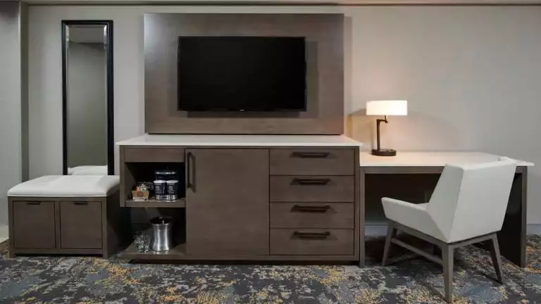 Interior of a room inside the Hilton Downtown Anchorage. White granite counter tops, a coffee machines, work station with chair. and long length wall mirror.