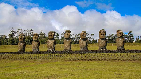 A line of moai stone statues with big heads, seen in a field of low-cut green grass on a sunny day during an adventure trip to Chile.