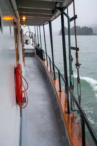 Looking out over a rainy Alaska landscape from the outer walk way that surrounds the main deck of Alaska small ship Catalyst.