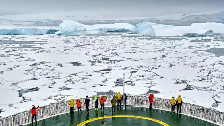 Guests on a Commandant Charcot Weddell Sea voyage stand on ship's helicopter launch pad bow & view a sea of icebergs.