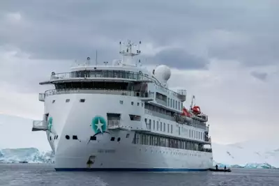 Exterior view of the modern Antarctic expedition ship Greg Mortimer, white and futuristic looking as it cruises the ocean.