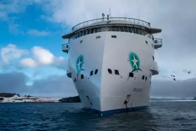 Frontal exterior view of the modern Greg Mortimer ship, white and futuristic looking as it cruises the ocean.