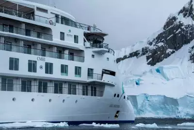 The front exterior of modern Greg Mortimer ship, futuristic and white with decks of windows and wrap around walkways.
