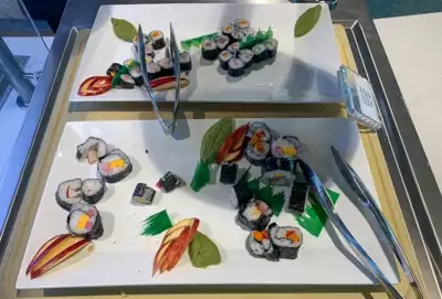 Two white serving plates filled with colorful sushi rolls and metals tongs, part of buffet dinner aboard Greg Mortimer ship.