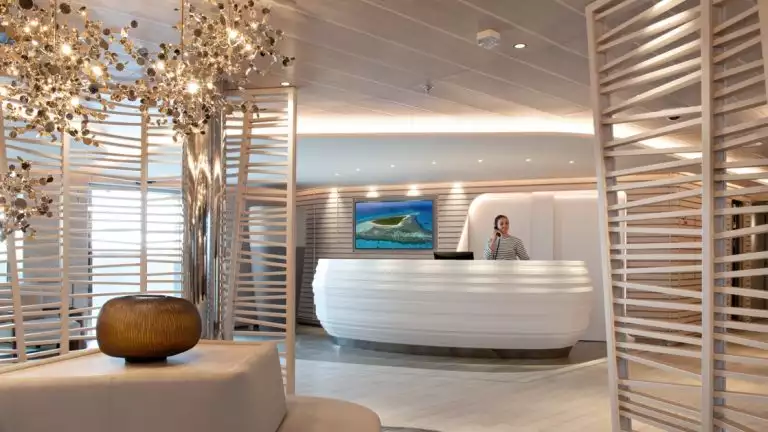 Woman in nautical shirt stands behind a large white desk, talking on the phone, in glamorous reception area of Le Bellot small ship.
