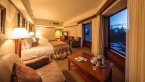 Hotel Alyeska Junior Suite with 2 double beds, padded chairs, TV, wooden coffee table & dresser, beige & tan accents & wraparound windows.
