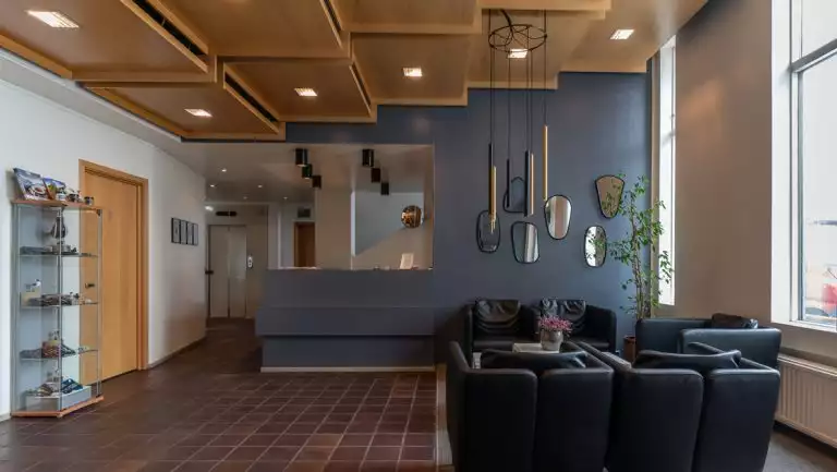 Lobby of Iceland Hotel Isafjordur, with wood floors, glass bookshelf with handicrafts, recessed lighting in cascading wood boxes, & black leather couches.
