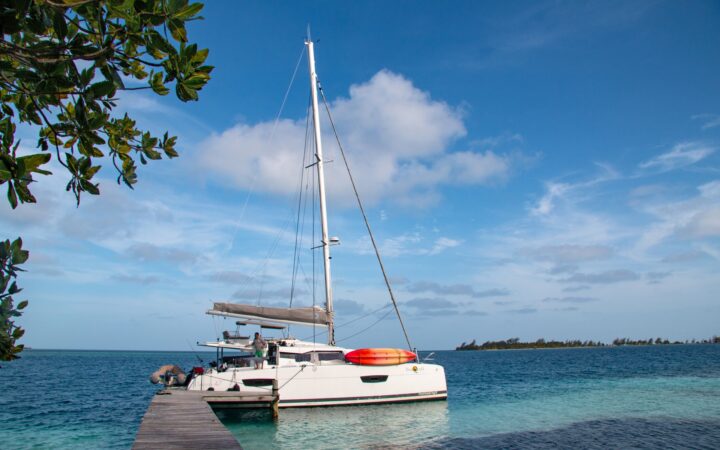 A wooden dock stretches into the teal blue ocean water of Belize, a bright while sailboat floats at the end waiting for its guests.