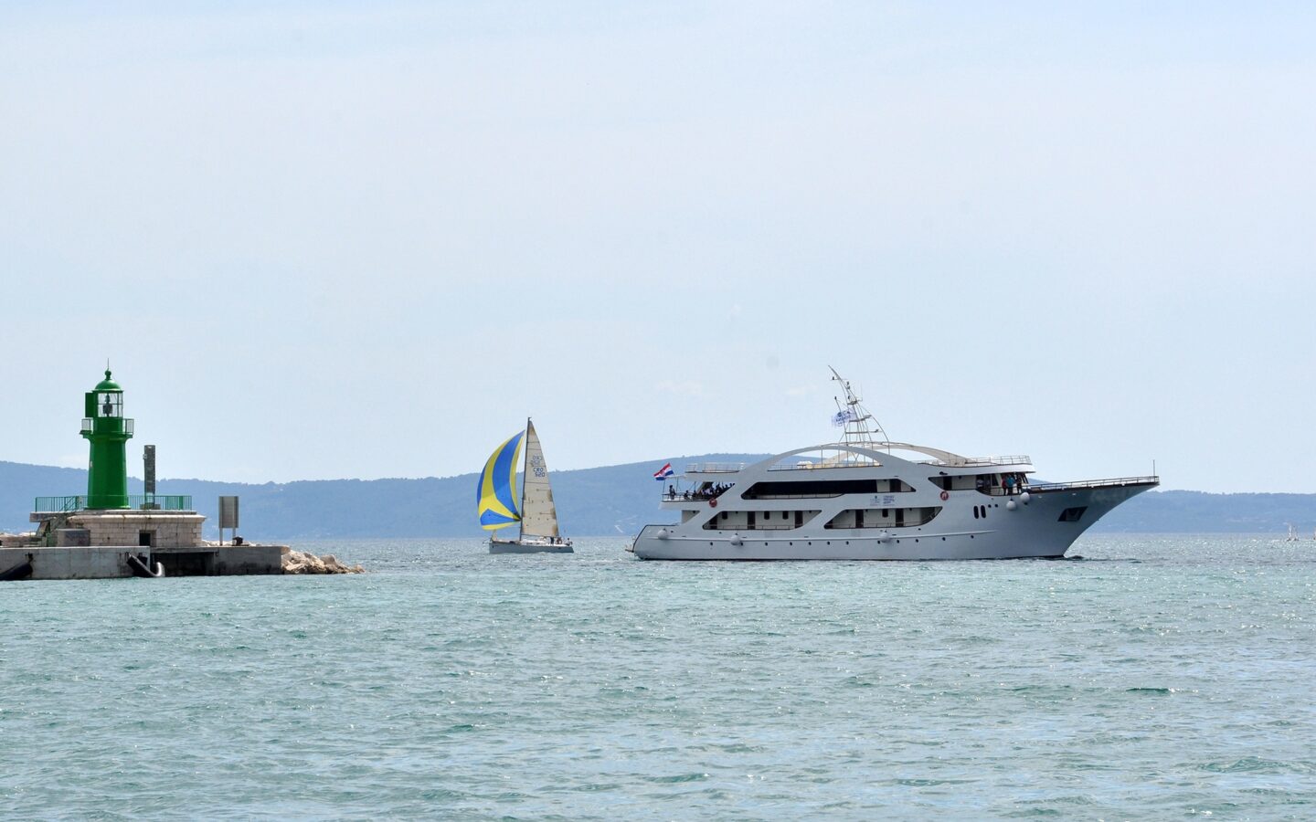 A Mediterranean yacht charter boat seen cruising beside a sailboat and a lighthouse