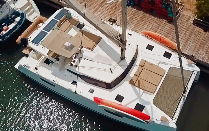 Aerial drone photo of the exterior of Tranquilo, a white Belize catamaran sailboat tied up at a wooden dock.