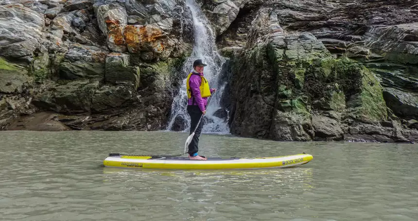 Woman paddles a yellow stand-up paddleboard while inside passage whale watching in Alaska.